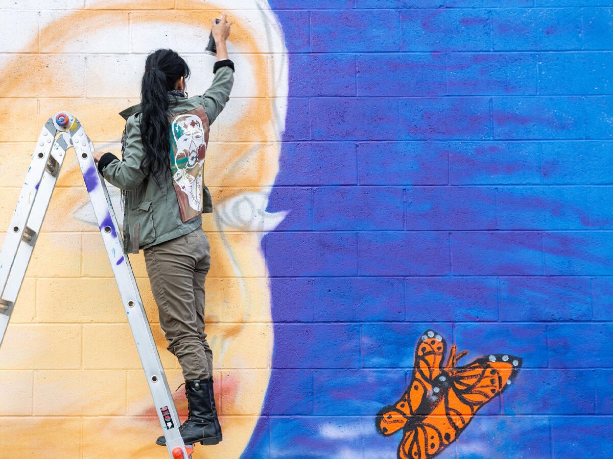 student on a ladder painting a mural